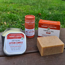 A certified organic and plastic free outdoor gift set including a bug repellent lotion bar stick, a camping soap bar and a bug repellent lotion candle.